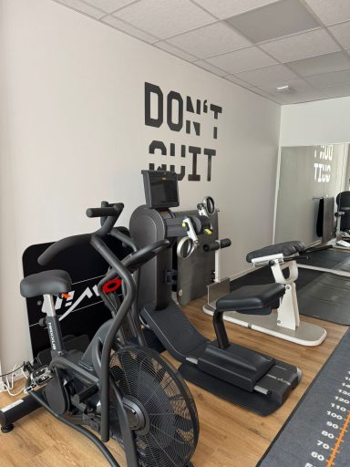 Fitnessstudio mit Trainingsgeräten und einem motivierenden Wandtext „DON'T QUIT“.
