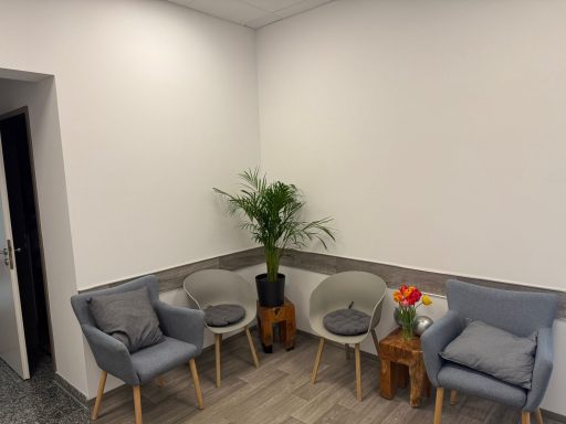 Heller Wartebereich mit grauen Sesseln, Pflanzen und einem kleinen Tisch.